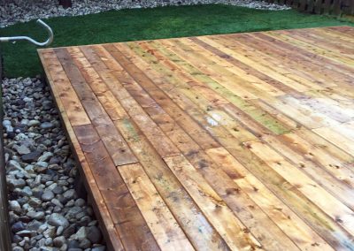 Wooden deck design surrounded by decorative rocks and grass in residential backyard