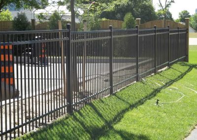 Commercial iron fence and wooden fence surrounded by grass and a parking lot
