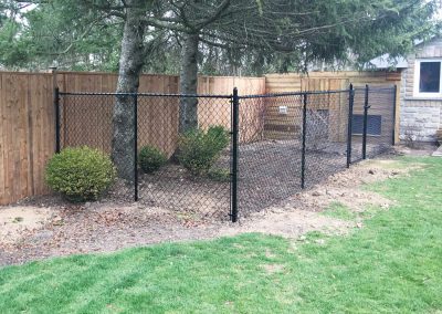Residential black chain-link fence in a backyard that's enclosing trees and bushes